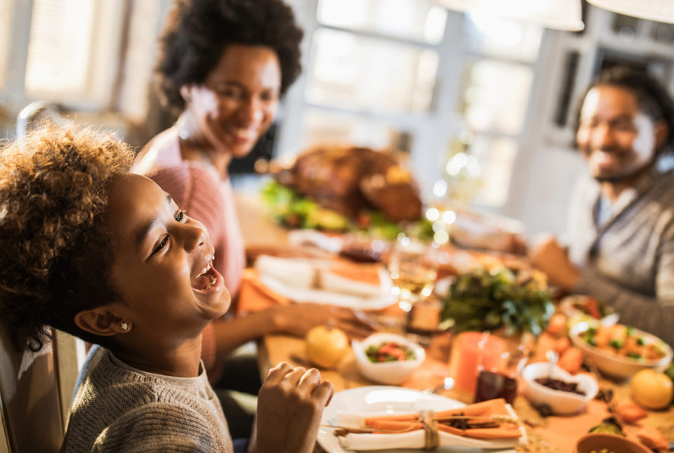 Cheerful girl laughing while having a meal with her parents in dining room.