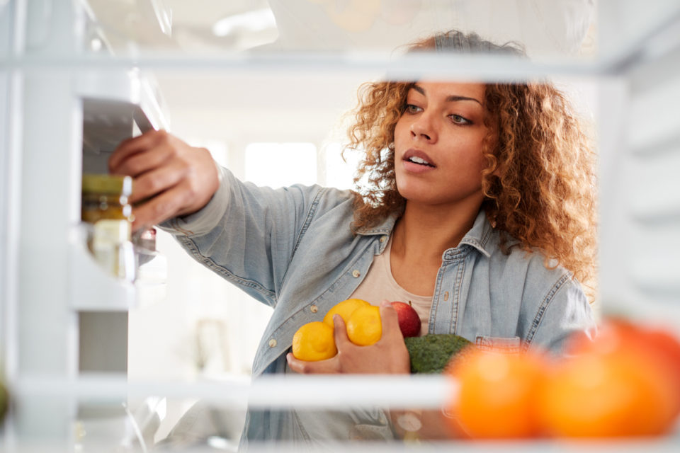 View Looking Out From Inside Of Refrigerator As Woman Opens Door And Packs Food Onto Shelves