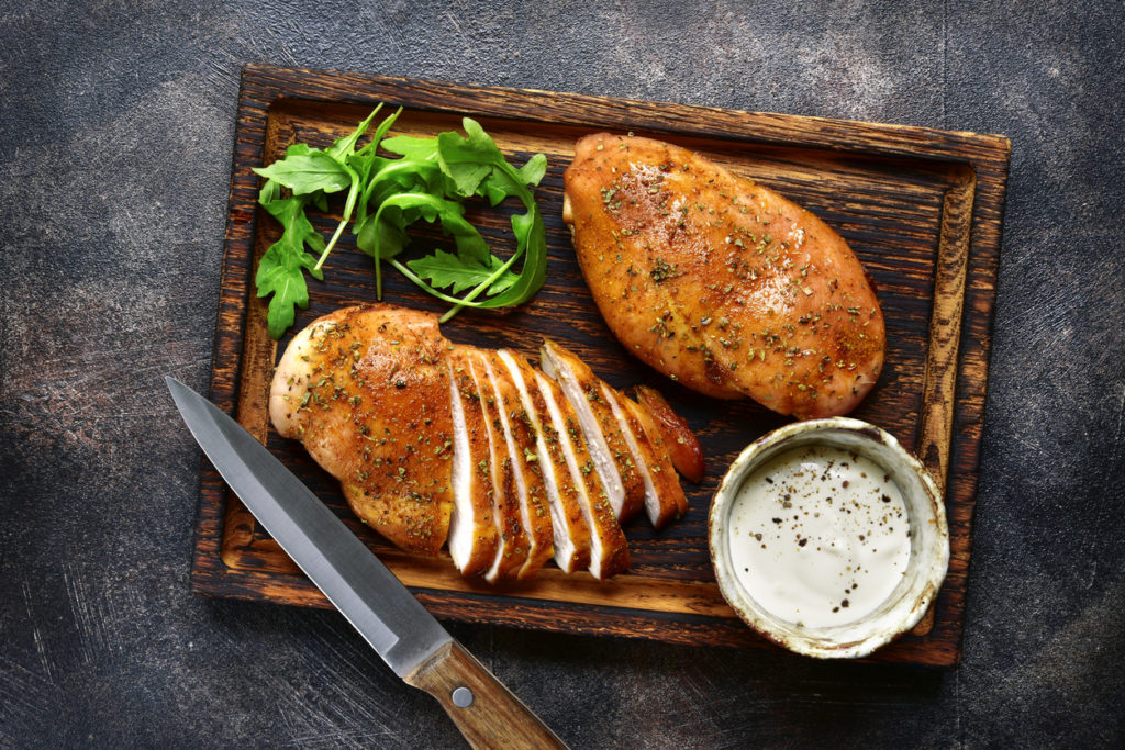 seared and cut chicken on a cutting board with garnish and a knife