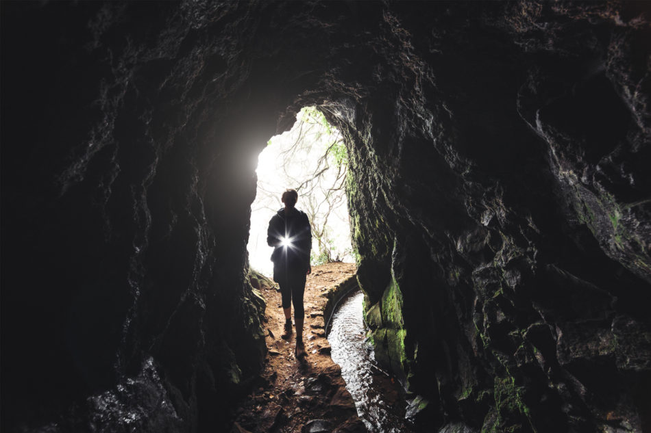 Woman walking into cave with a flashlight