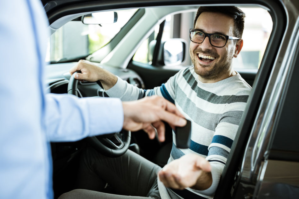 Young happy man receiving new car keys in a showroom