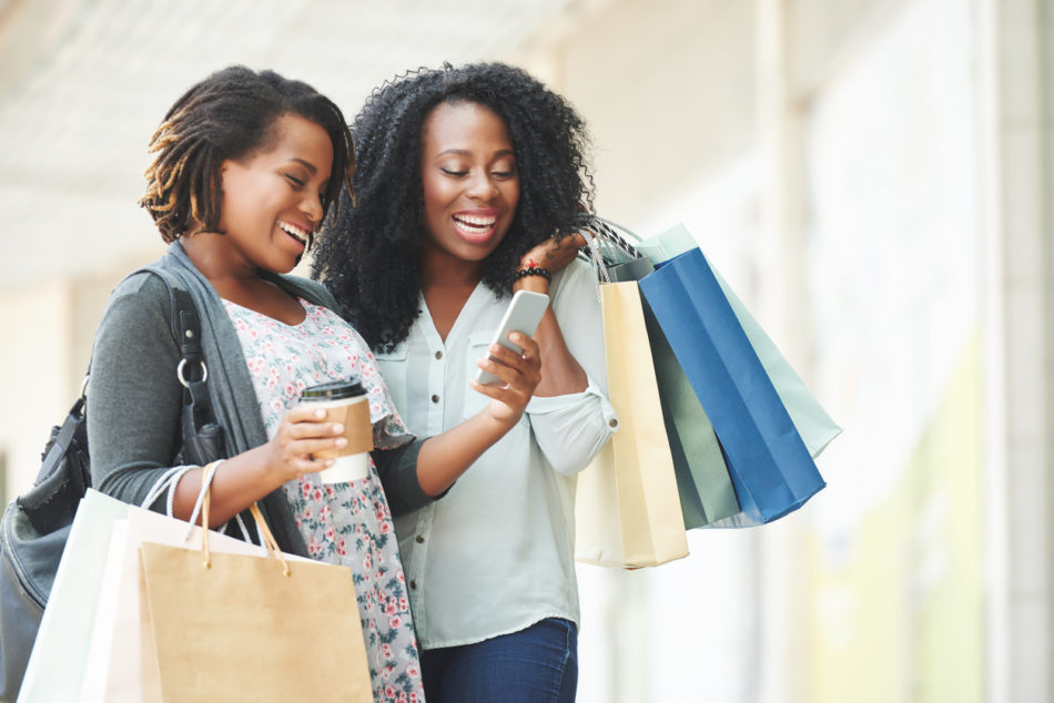 women holding shopping bags and reading a message off a phone